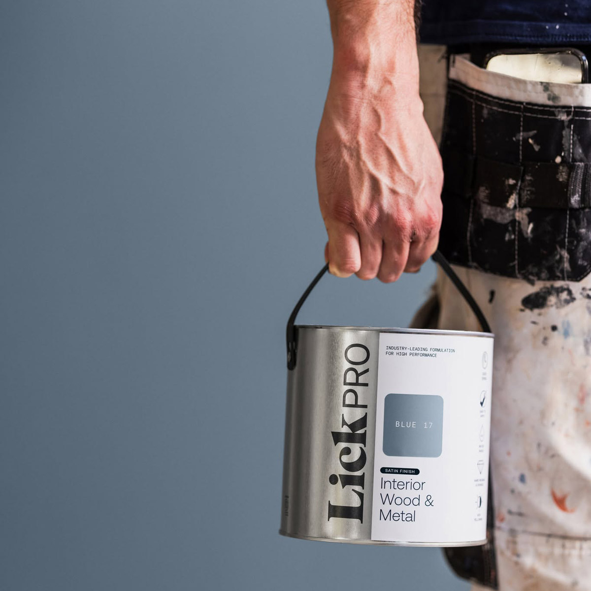 Decorator holding a can of LickPro Interior Wood & Metal paint by their side.
