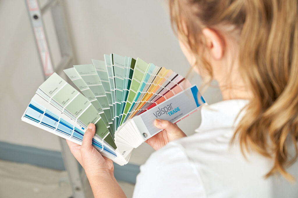 Looking over the shoulder of a female decorator who is examining a colour fandeck, or swatch.